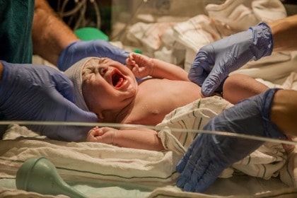 doctor and nurse gloved hands touching newborn infant