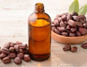 bottle of jojoba oil and seeds in wooden bowl