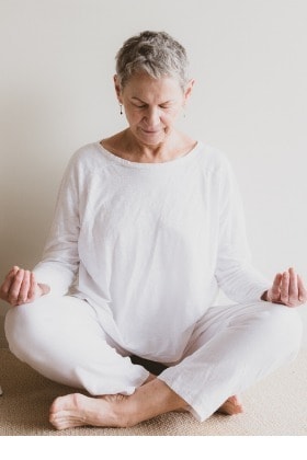 mature-woman-in-white-clothing-sitting-in-yoga-meditation-position