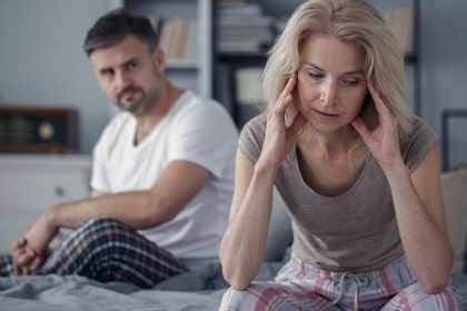 unhappy-woman-sitting-on-end-of-bed-husband-looking-at-her