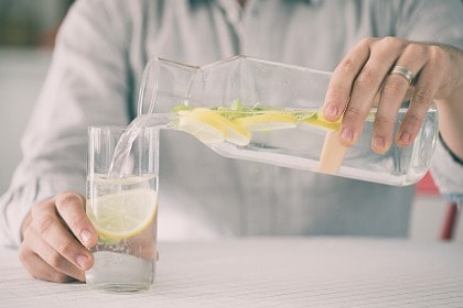 young-man-pouring-water-with-lemon-from-bottle-to-glass-in-kitchen