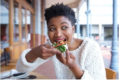 young-woman-eating-meal-taking-bite-of-food-outside-at-restaurant-