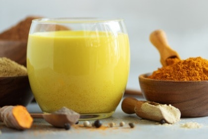 turmeric golden milk with turmeric root and bowl of ground turmeric powder commonly used in Ayurvedic medicine