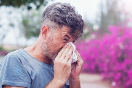 man-sneezing-in-a-tissue-outdoors-blowing-nose-pollen-allergy