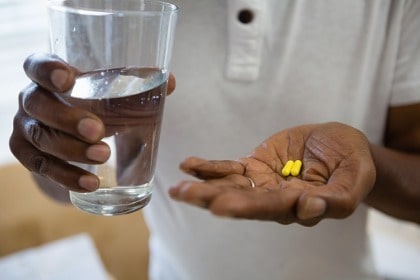mid-section-of-senior-man-holding-medicine-supplement-pill-and-drinking-water