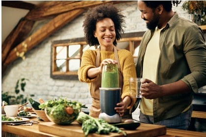 happy-couple-preparing-healthy-smoothie-in-kitchen-with-leafy-greens