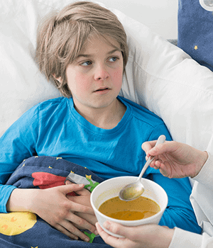 Boy sick in bed being fed broth