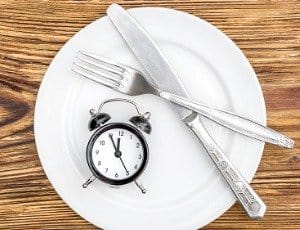 empty plate on table with knife, fork, and alarm clock