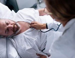 doctor checking heart rate of male patient in hospital bed