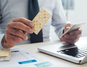 businessman holding saltine cracker in one hand and phone in other