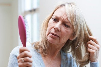 woman looking at hair brush concerned about hair loss