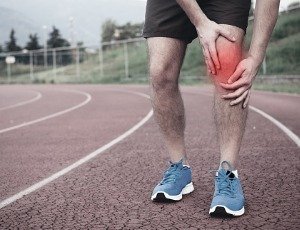 man holding painful knee on running track