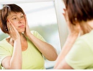 woman looking in mirror pulling back sagging skin